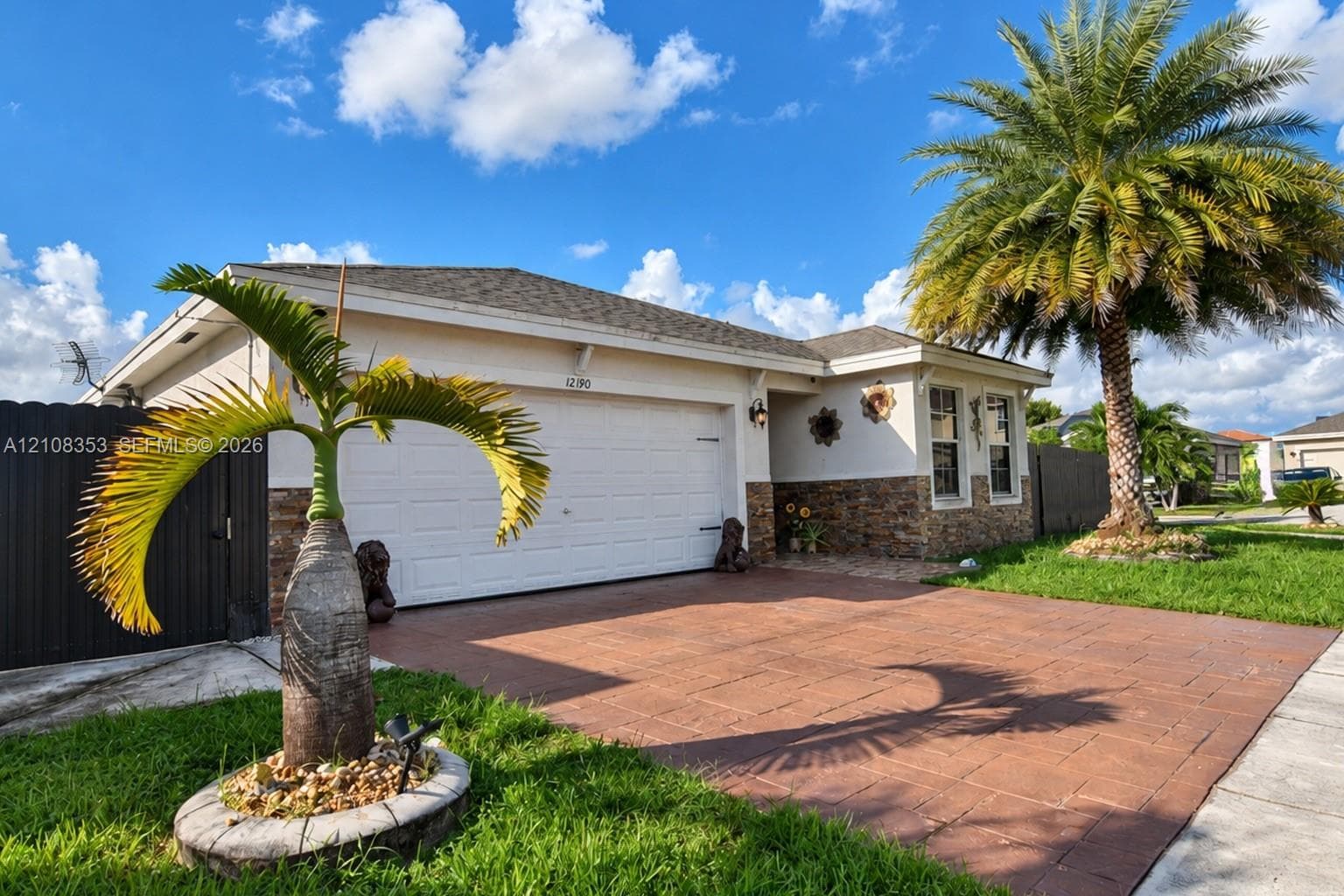 Single-story residence featuring a multi-textured exterior of light-toned stucco and masonry stone veneer, a stamped concrete driveway, a two-car garage, and established palm landscaping