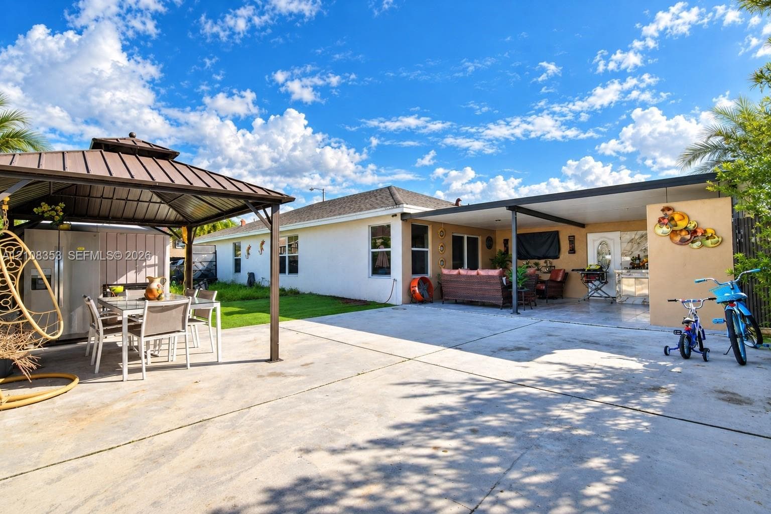 Exterior space featuring a concrete patio, a metal-roof gazebo, a covered porch, and a manicured lawn