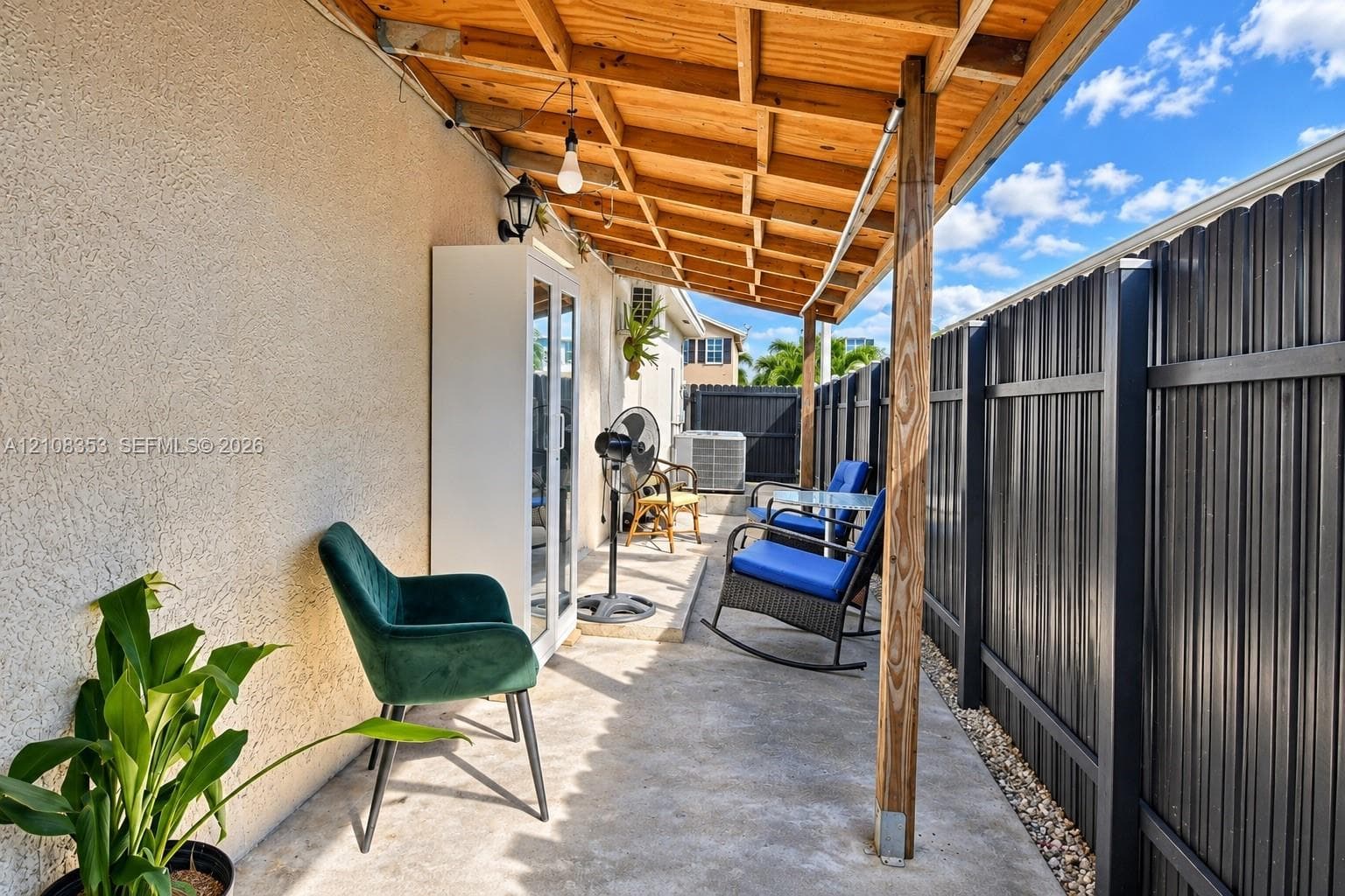 Covered patio featuring a concrete surface, exposed wood-beam ceiling, and black metal vertical-slat fencing