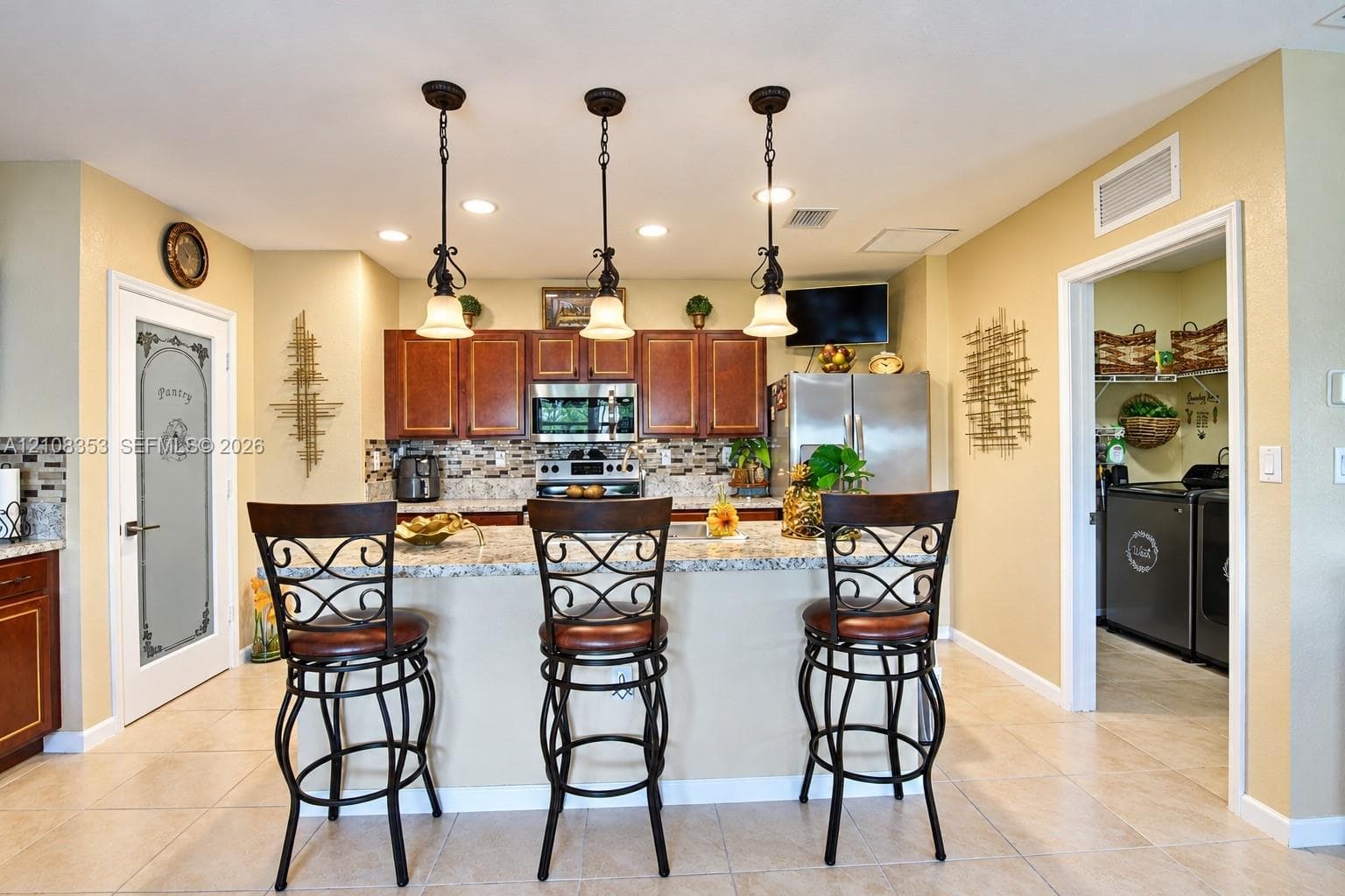 Kitchen featuring stained wood cabinetry, stone countertops, mosaic tile backsplash, three-light pendant fixture, and a pantry with a decorative glass door
