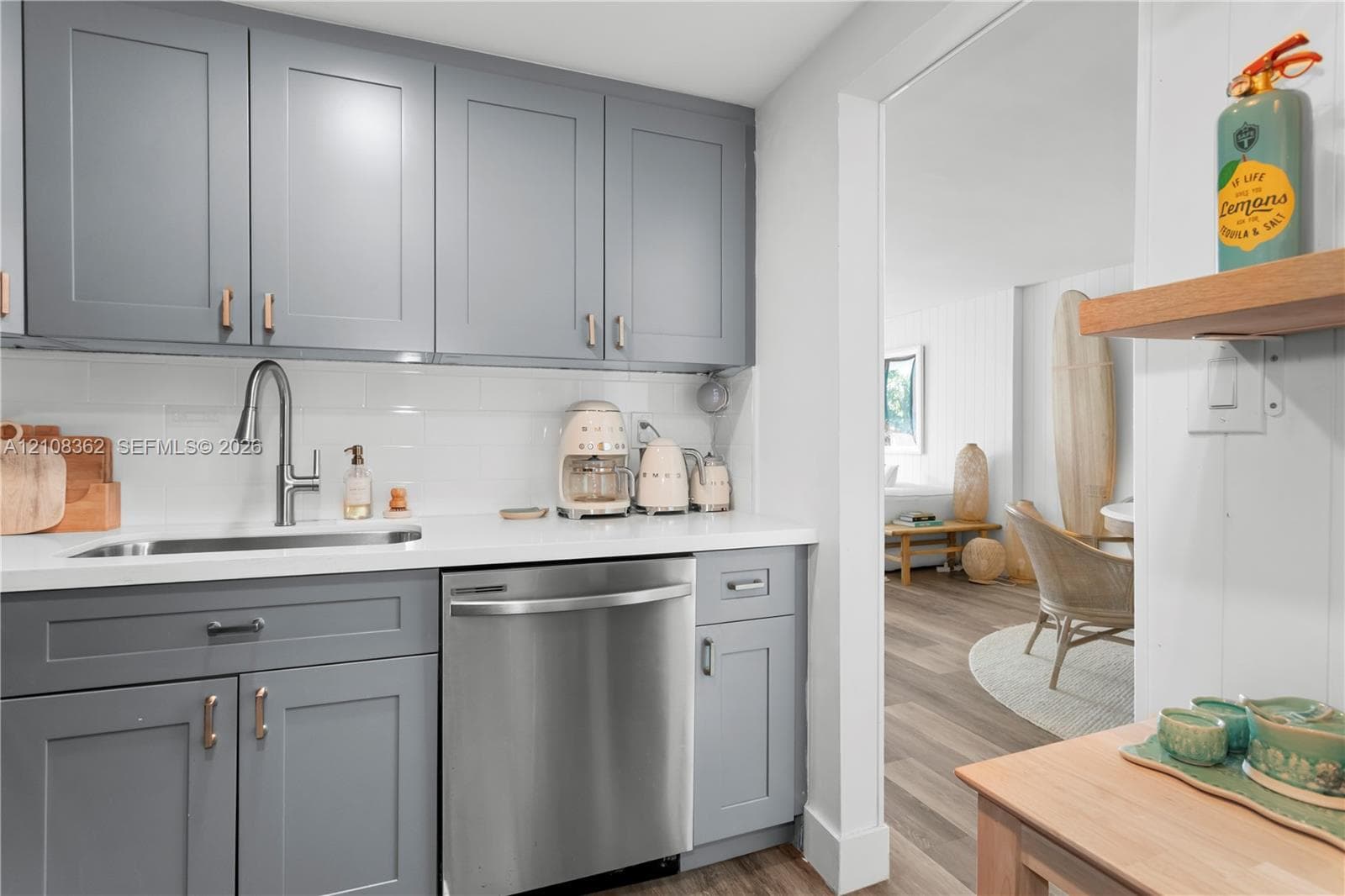 Kitchen featuring grey shaker-style cabinetry, white subway tile backsplash, solid-surface countertops, undermount stainless steel sink with pull-down faucet, and built-in stainless steel dishwasher