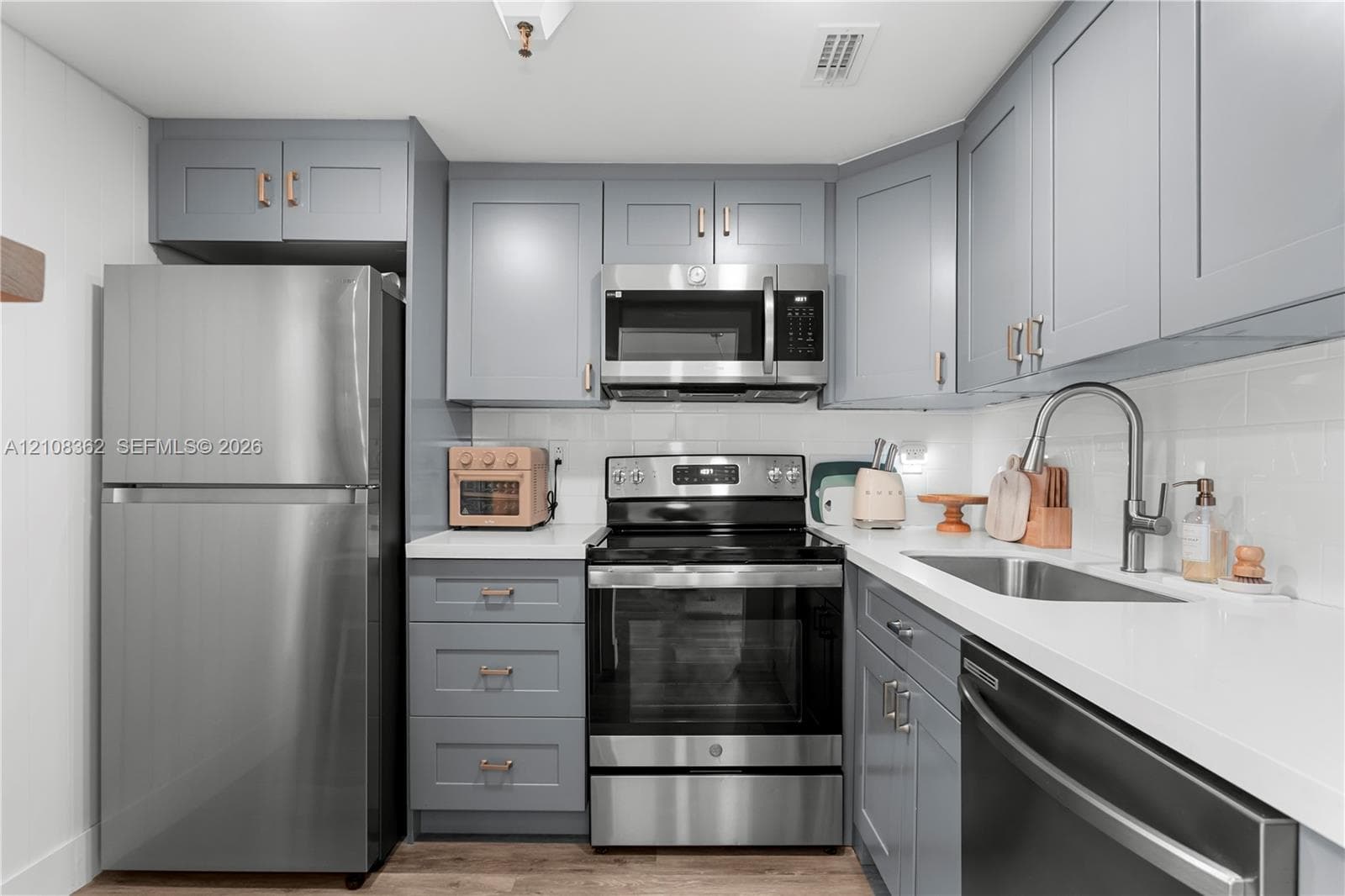 Kitchen featuring shaker-style cabinetry with metallic hardware, white solid-surface countertops, subway tile backsplash, and stainless steel appliances