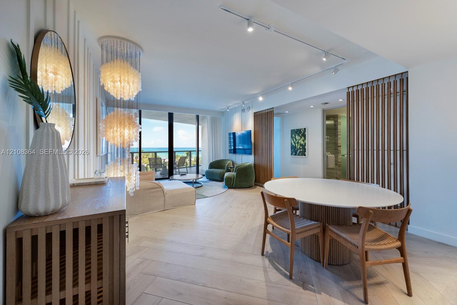 Herringbone wood-finish flooring, floor-to-ceiling glass balcony doors, decorative tiered pendant lighting, vertical wood slat wall detailing, and adjustable track lighting