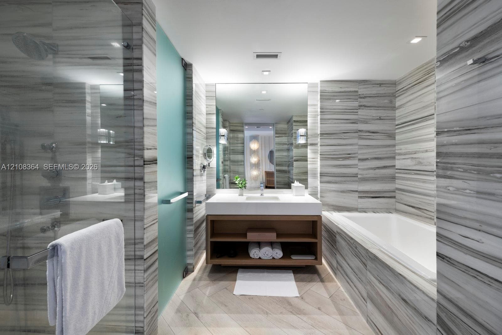 Bathroom featuring floor-to-ceiling stone tile, a soaking tub, a glass-enclosed shower, a floating wood-finish vanity, and recessed lighting