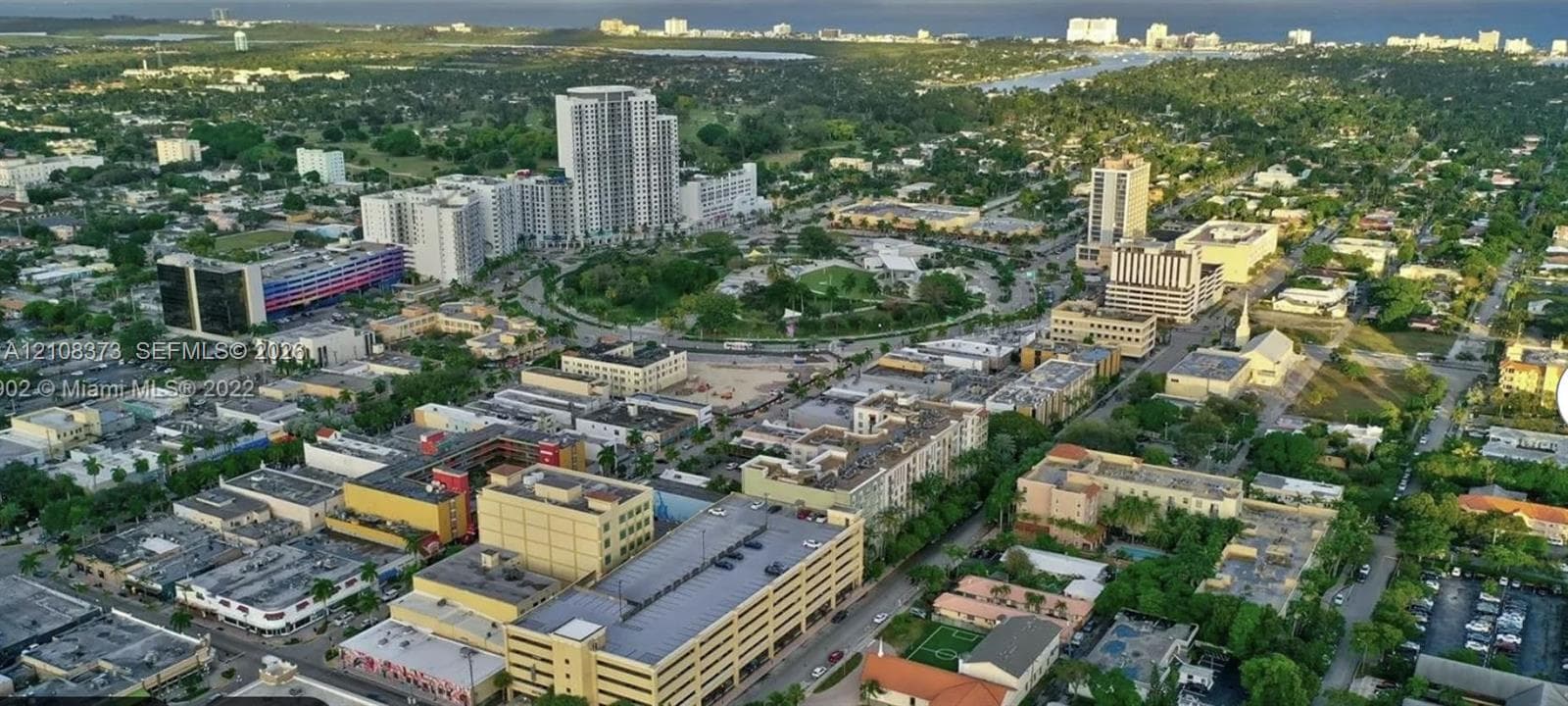 Aerial perspective of an urban district featuring high-rise architecture, mixed-use commercial buildings, dense mature tree canopy, and established thoroughfare infrastructure