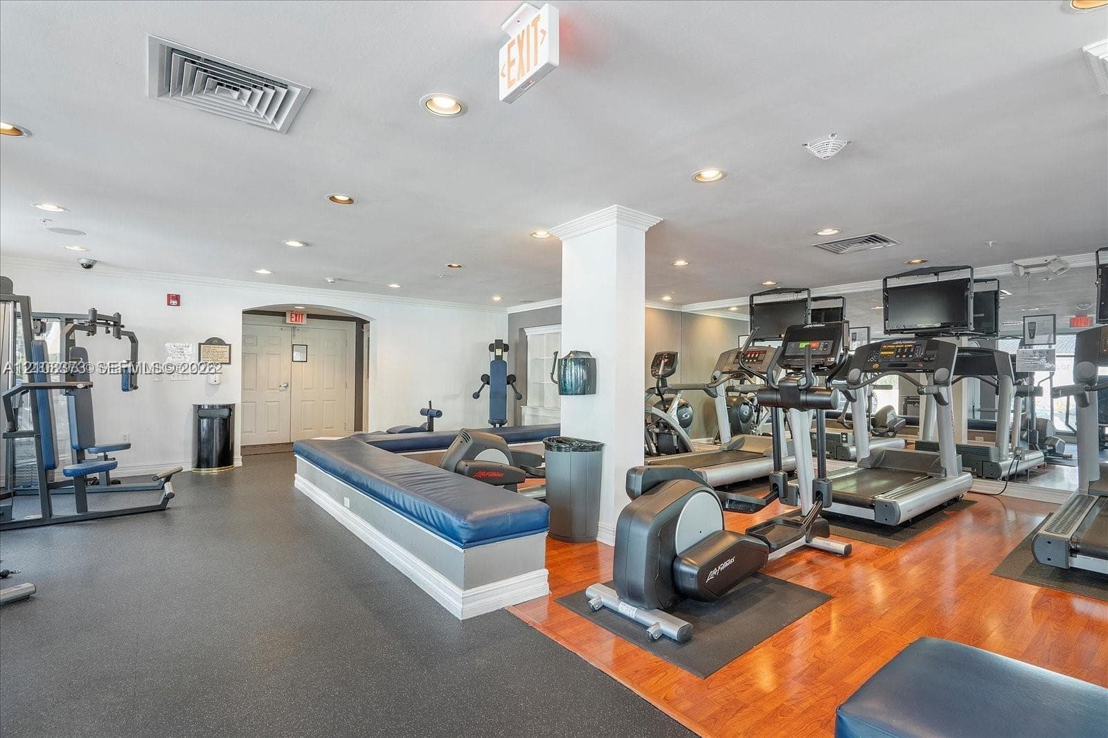 Fitness center featuring recessed lighting, expansive wall-to-wall mirrors, wood-finish flooring, and a built-in upholstered bench