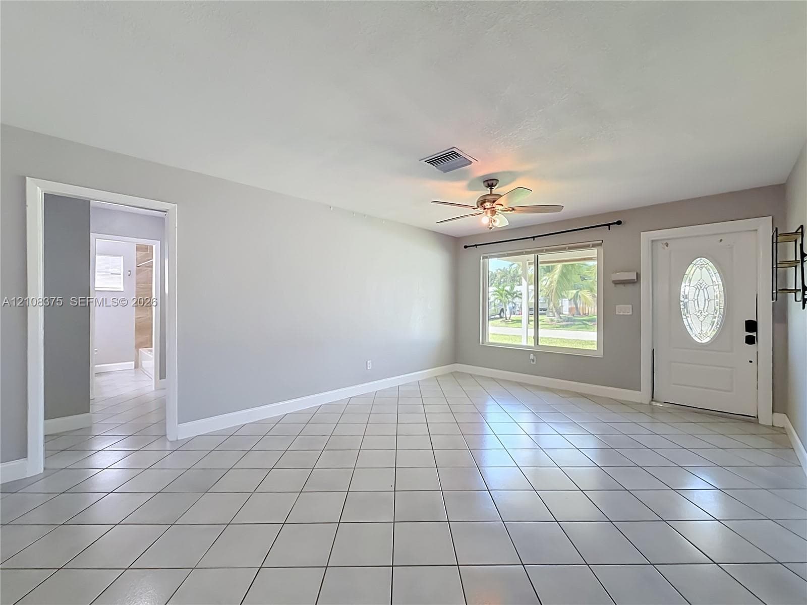 Neutral-toned interior space featuring white floor tiles, a ceiling fan with integrated lighting, and an entry door with an oval glass insert