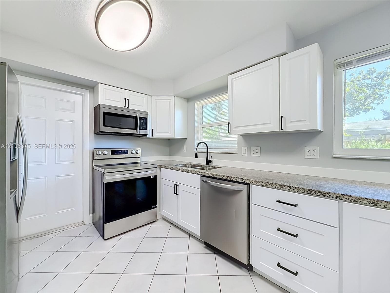 Kitchen featuring white shaker-style cabinetry, stone-finish countertops, stainless steel appliances, matte black hardware, and diagonal-set tile flooring