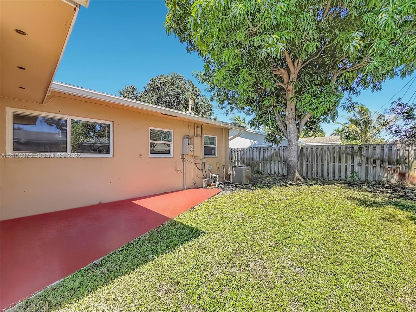 Rear exterior featuring a concrete patio, grassy yard, mature tree, and wood-panel privacy fencing