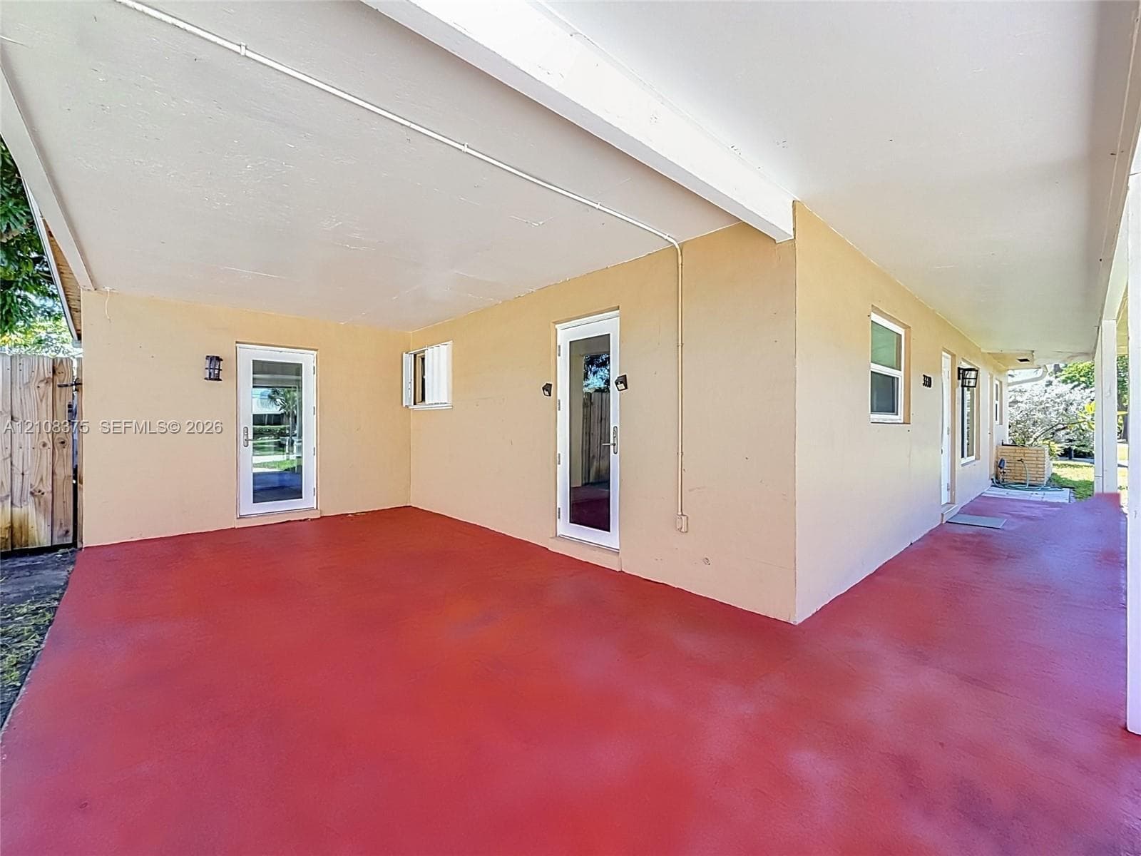 Covered patio with painted concrete flooring, stucco exterior walls, multiple glass-panel entry doors, and wall-mounted exterior light fixtures