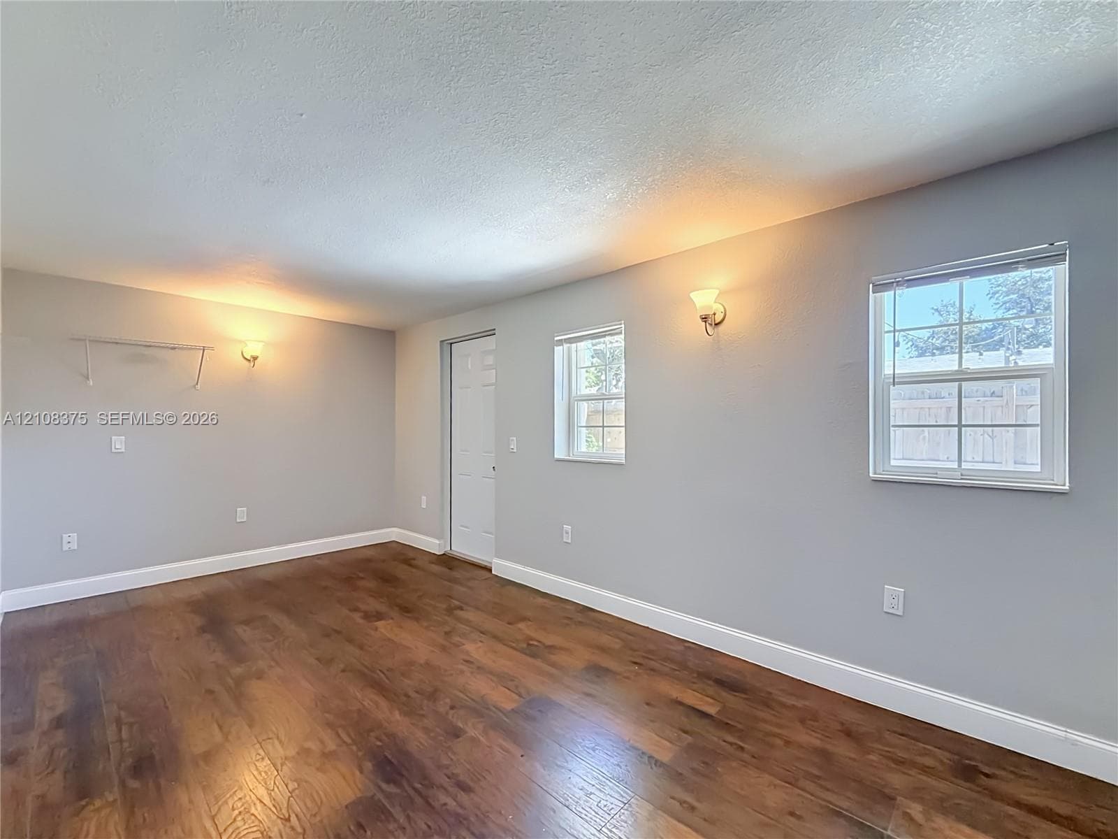 Interior space featuring wood-finish flooring, neutral wall tones, dual wall-mounted light fixtures, multi-pane windows, and a panel door