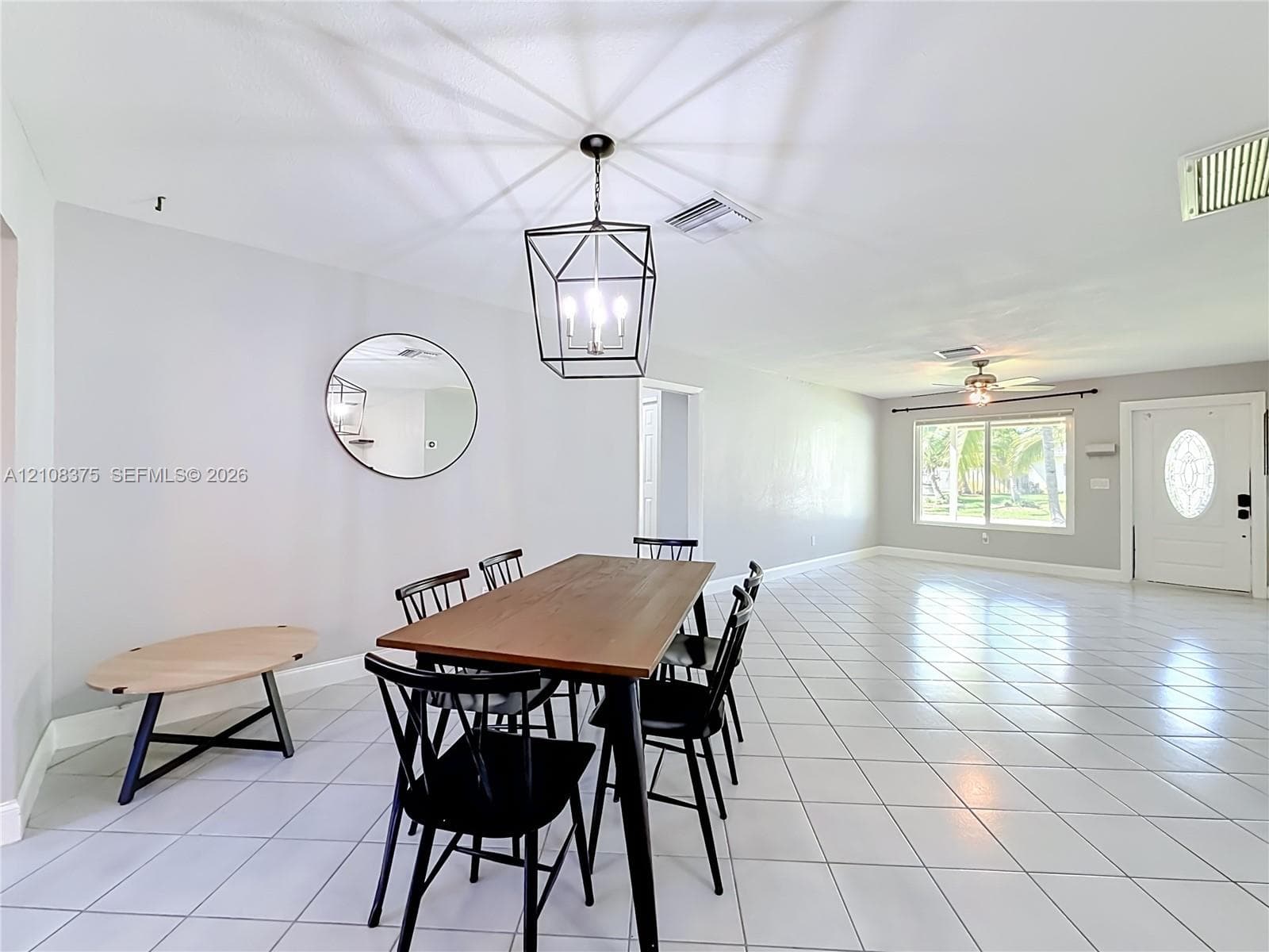 Large-format tile flooring, geometric metal cage pendant lighting, round wall mirror, and panel door with decorative glass insert