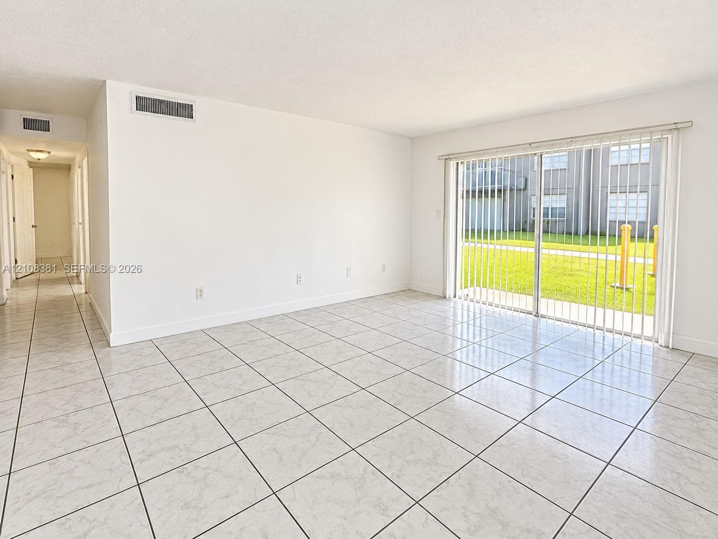 Neutral interior space featuring polished tile flooring, smooth white walls, and a large sliding glass door with vertical blinds