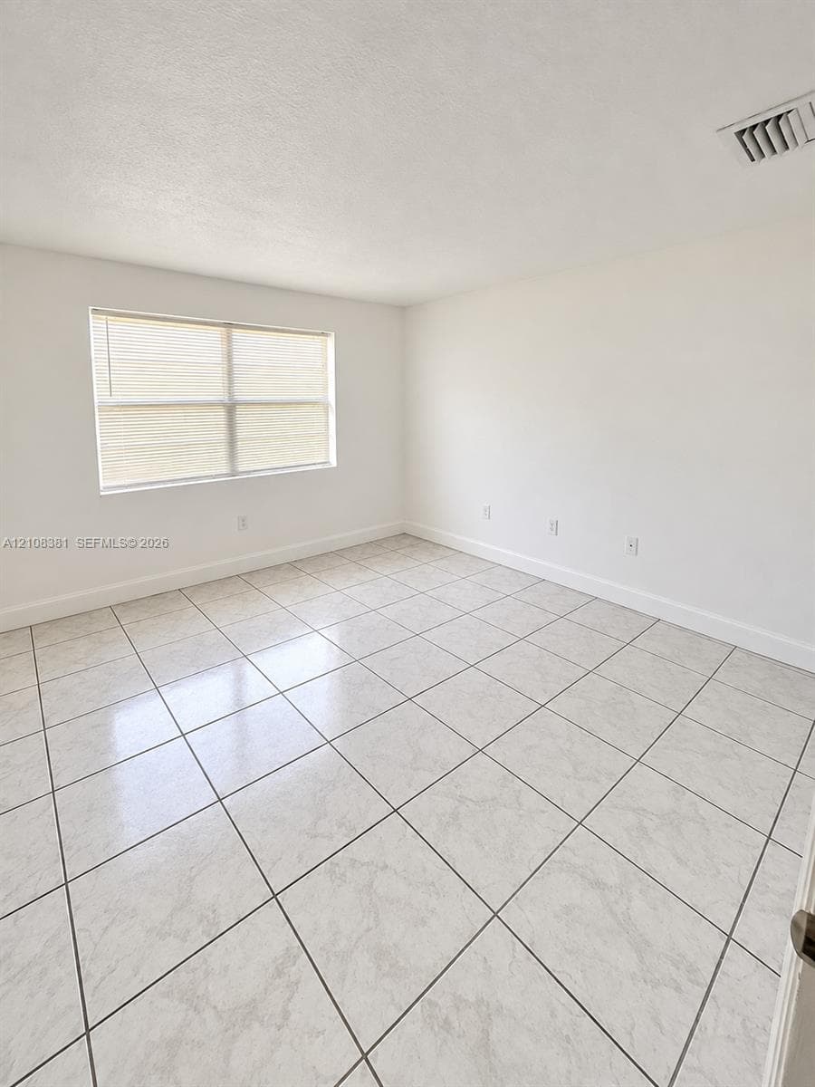 Neutral interior space featuring stone-finish tile flooring, white wall finishes, and a single window with blinds