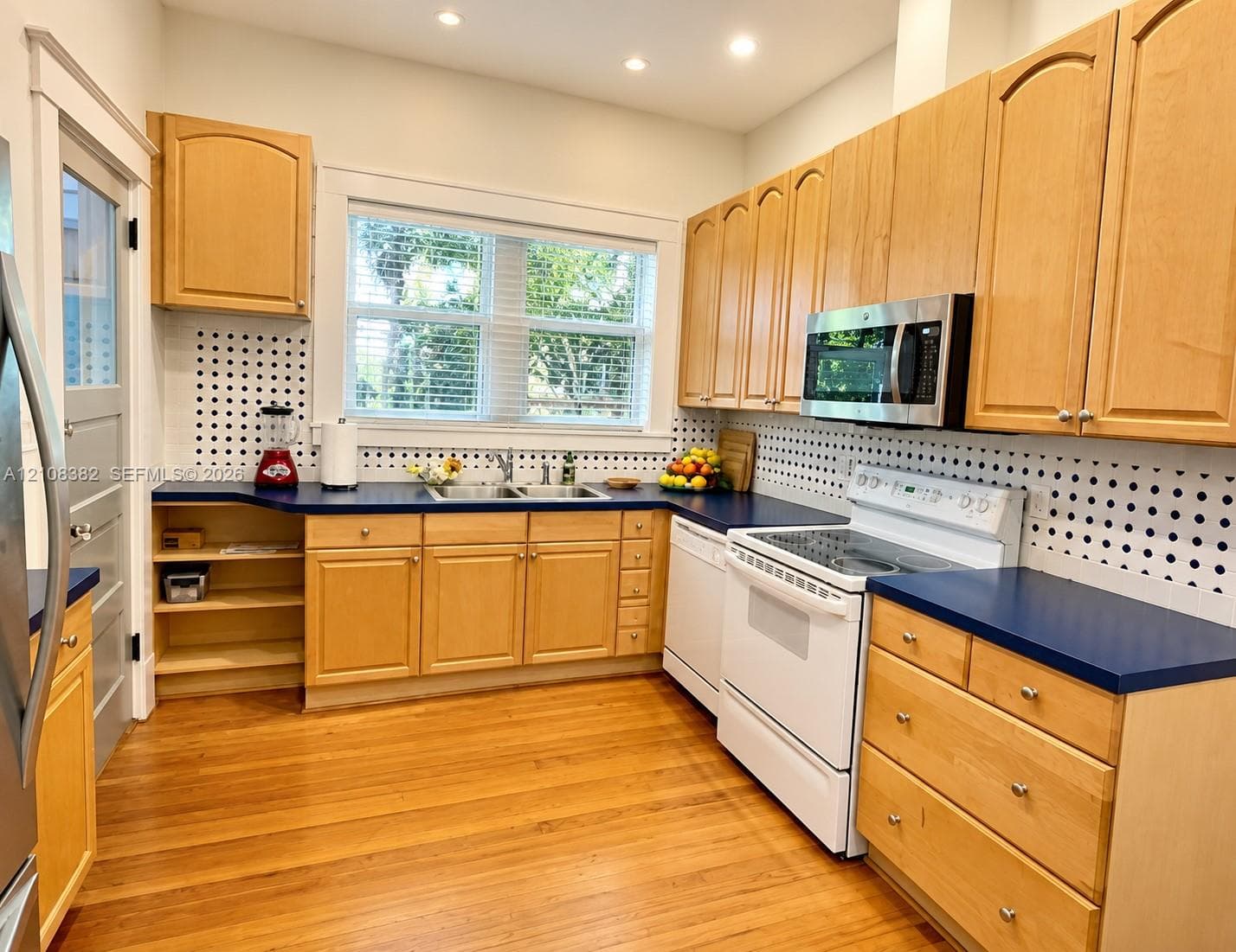 Kitchen featuring natural wood cabinetry, blue countertops, a double basin stainless steel sink, recessed lighting, and wood-finish flooring