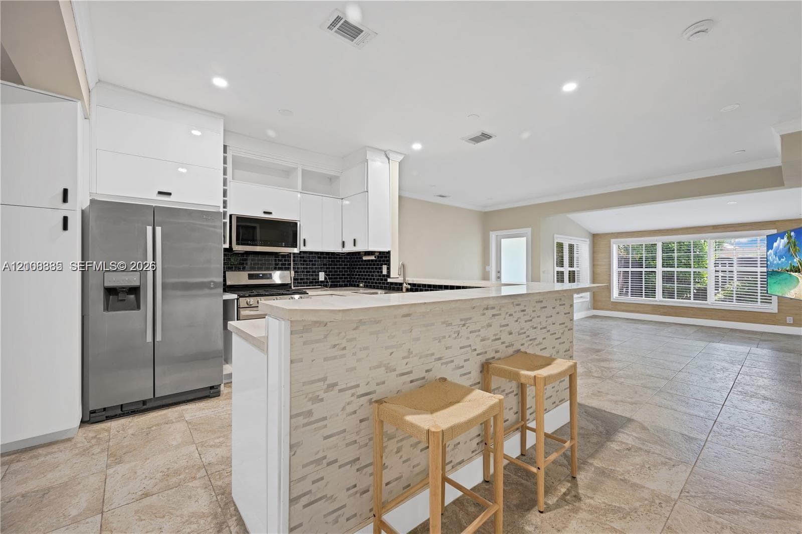 Kitchen featuring white flat-panel cabinetry, stainless steel appliances, a stone-tile breakfast bar, and tile flooring