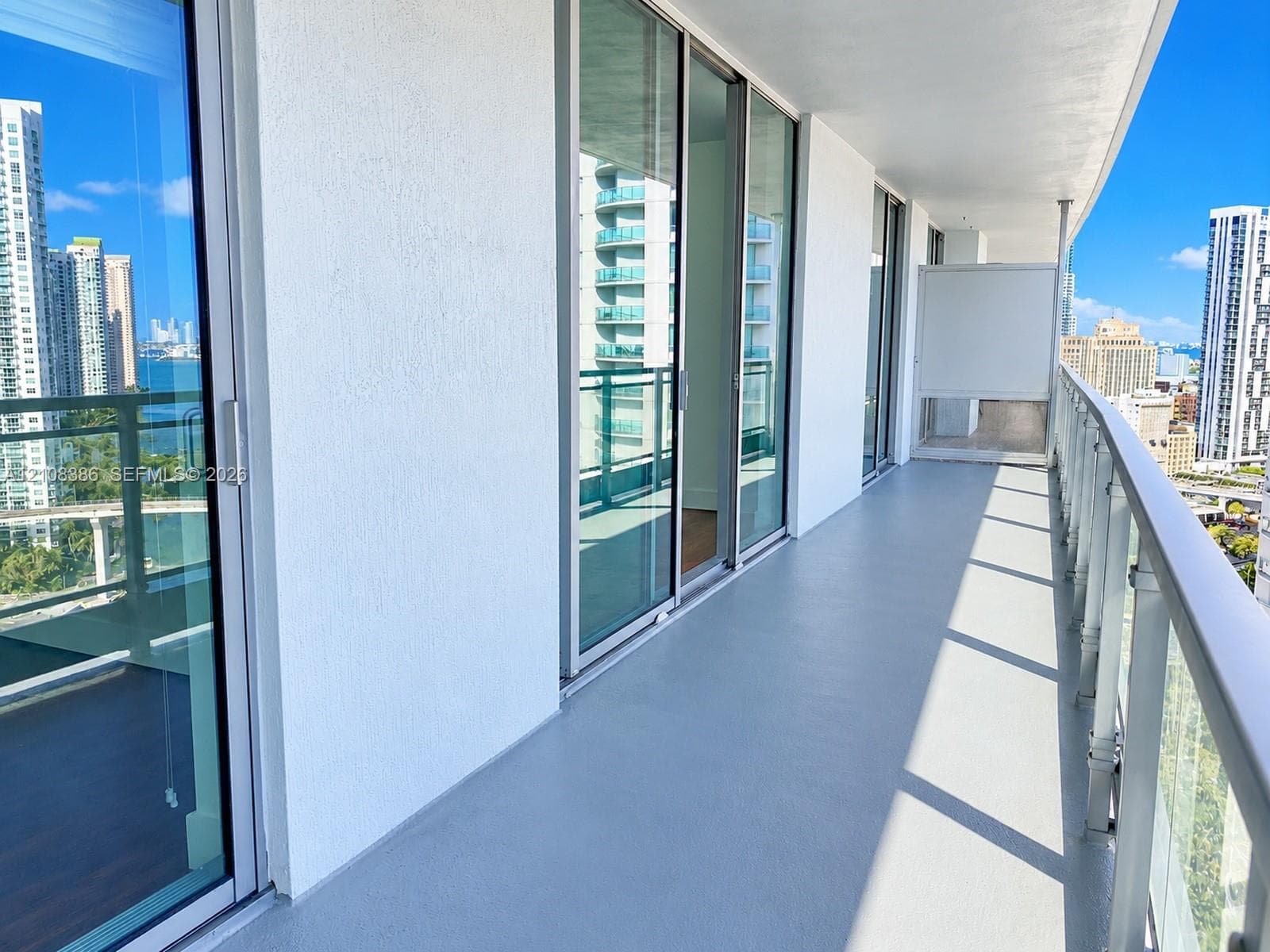 Covered outdoor balcony featuring full-height glass sliding doors, concrete flooring, and a glass-paneled railing
