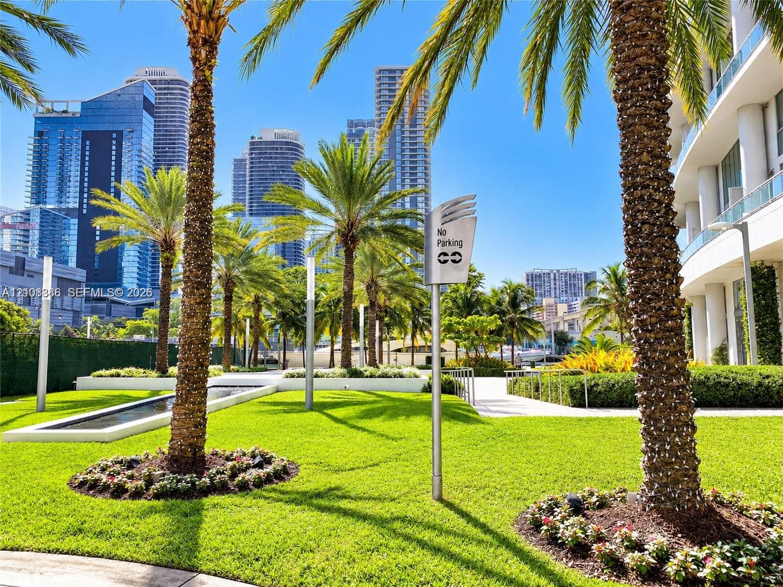 Landscaped grounds featuring mature palm trees, manicured lawns, a rectangular water feature, and paved walkways