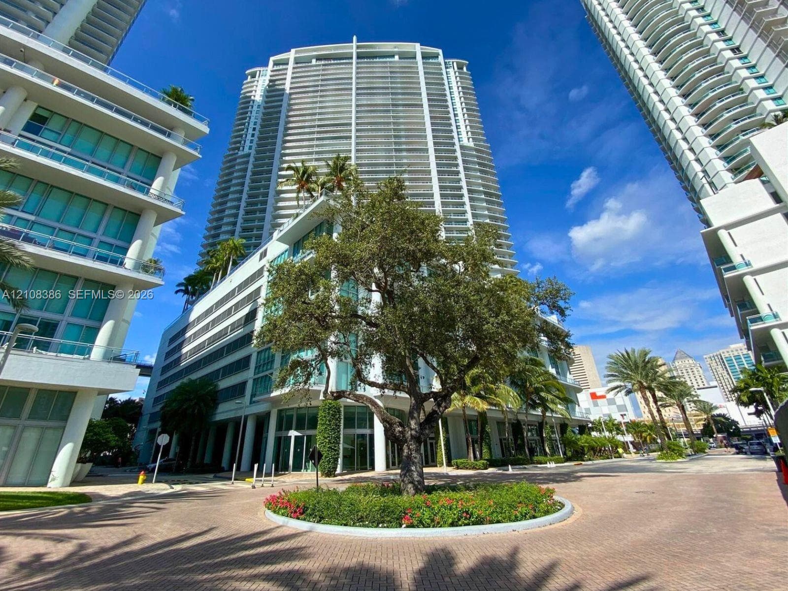 High-rise building featuring a glass and concrete exterior, extensive balcony levels, and a circular paved motor court with mature landscaping