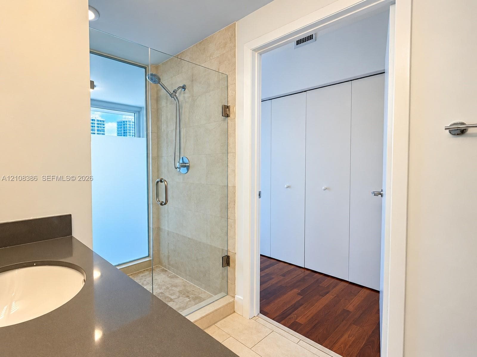 Walk-in shower with a glass enclosure and neutral-toned tile, vanity with a dark-toned countertop and integrated sink, and built-in closet cabinetry with wood-finish flooring