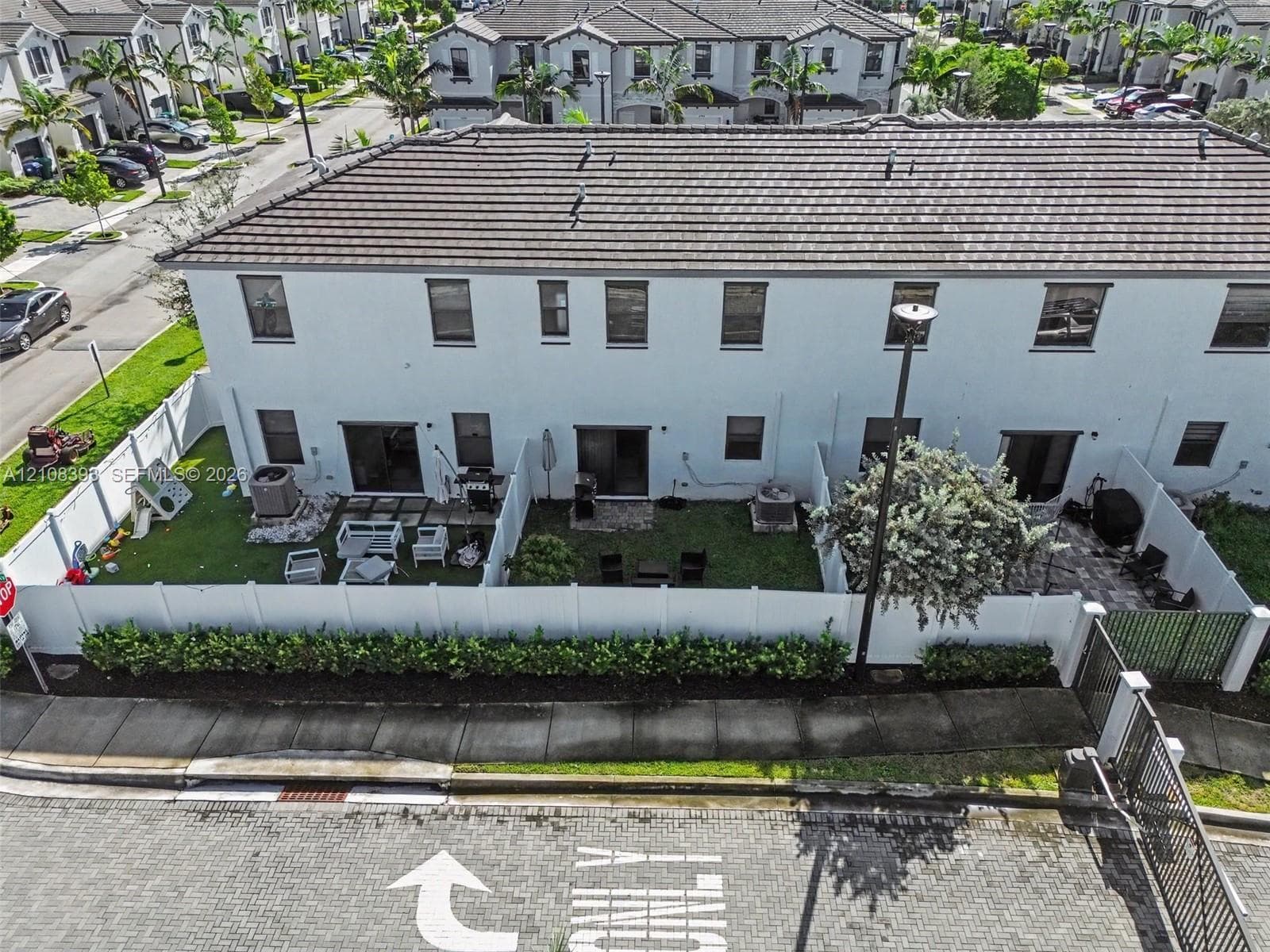 Two-story townhouse exterior featuring white stucco siding, a tiled roof, private fenced rear yards with patio pavers, and manicured landscaping