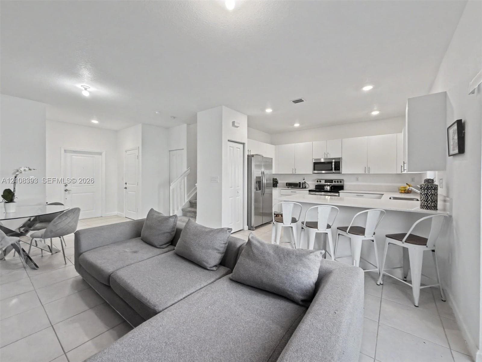 Open-concept kitchen featuring white cabinetry, a spacious central island with bar seating, stainless steel appliances, and neutral tile flooring throughout