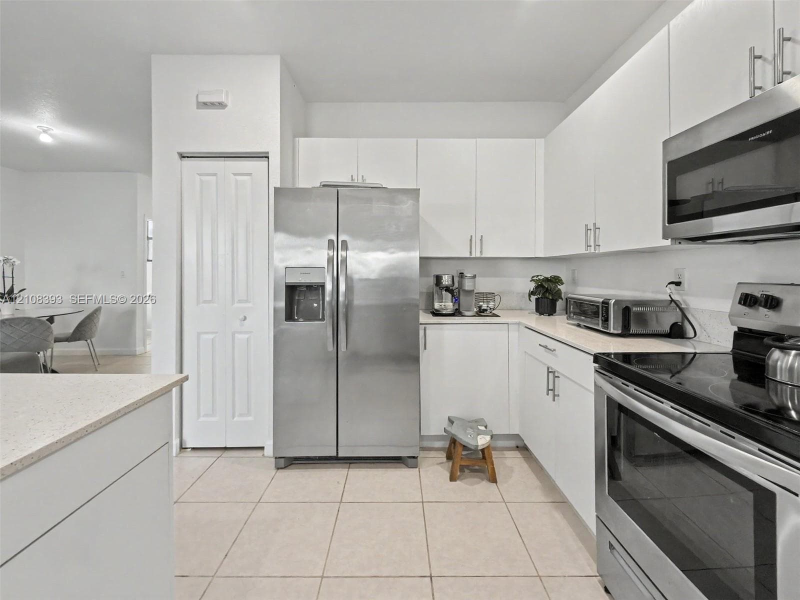 Kitchen featuring white cabinetry, light-colored countertops, tile flooring, and stainless steel appliances including a refrigerator and over-the-range microwave