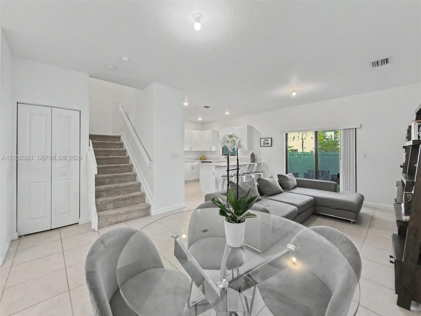 Open-concept interior featuring neutral tile flooring, recessed lighting, carpeted staircase with white balusters, white cabinetry, and sliding glass doors