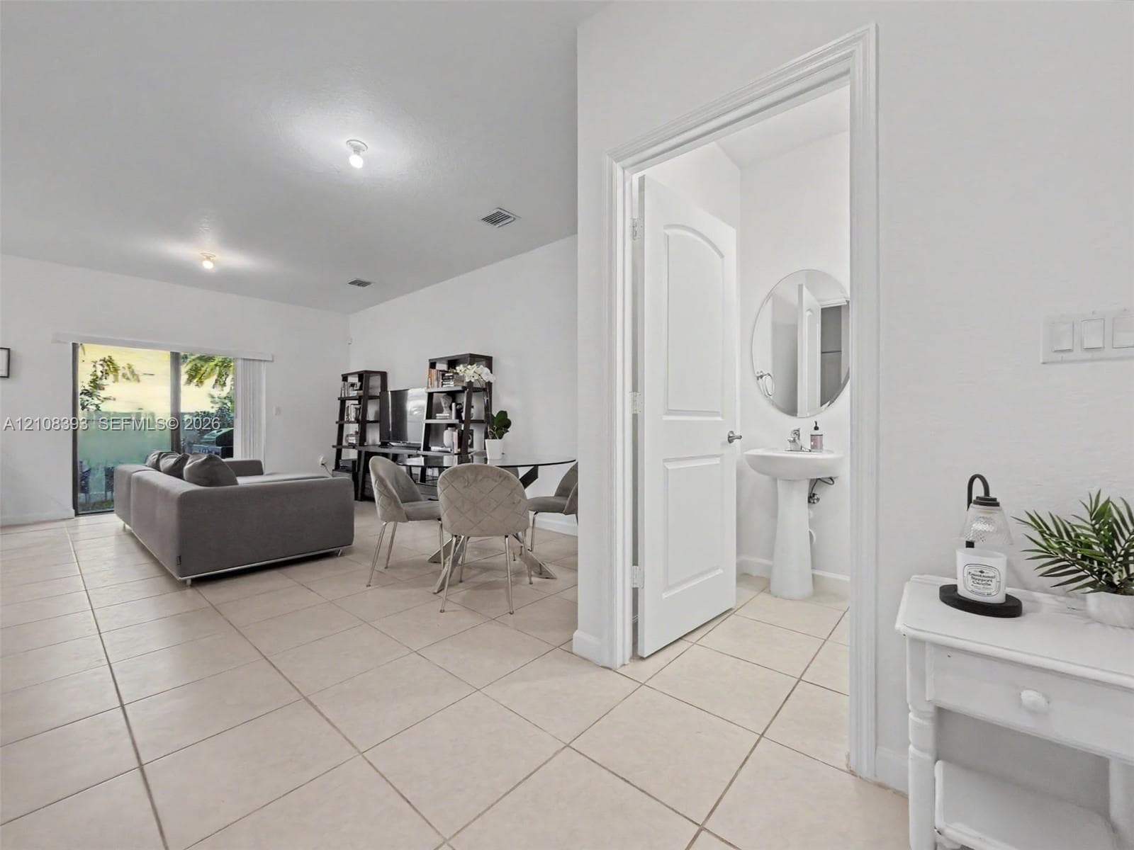 Neutral-tone tile flooring, sliding glass door, and a pedestal sink with a circular wall mirror