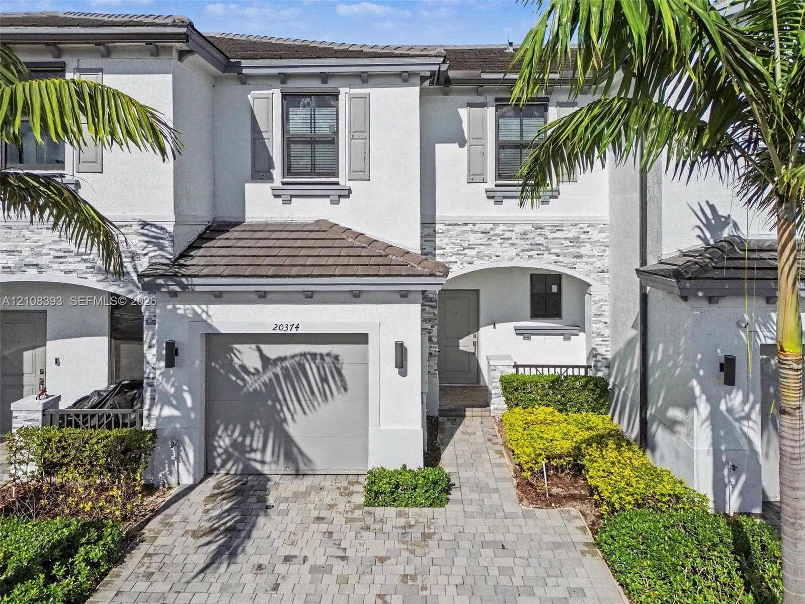 Exterior facade featuring stucco siding, stone veneer accents, concrete tile roofing, shutters, and a paver driveway