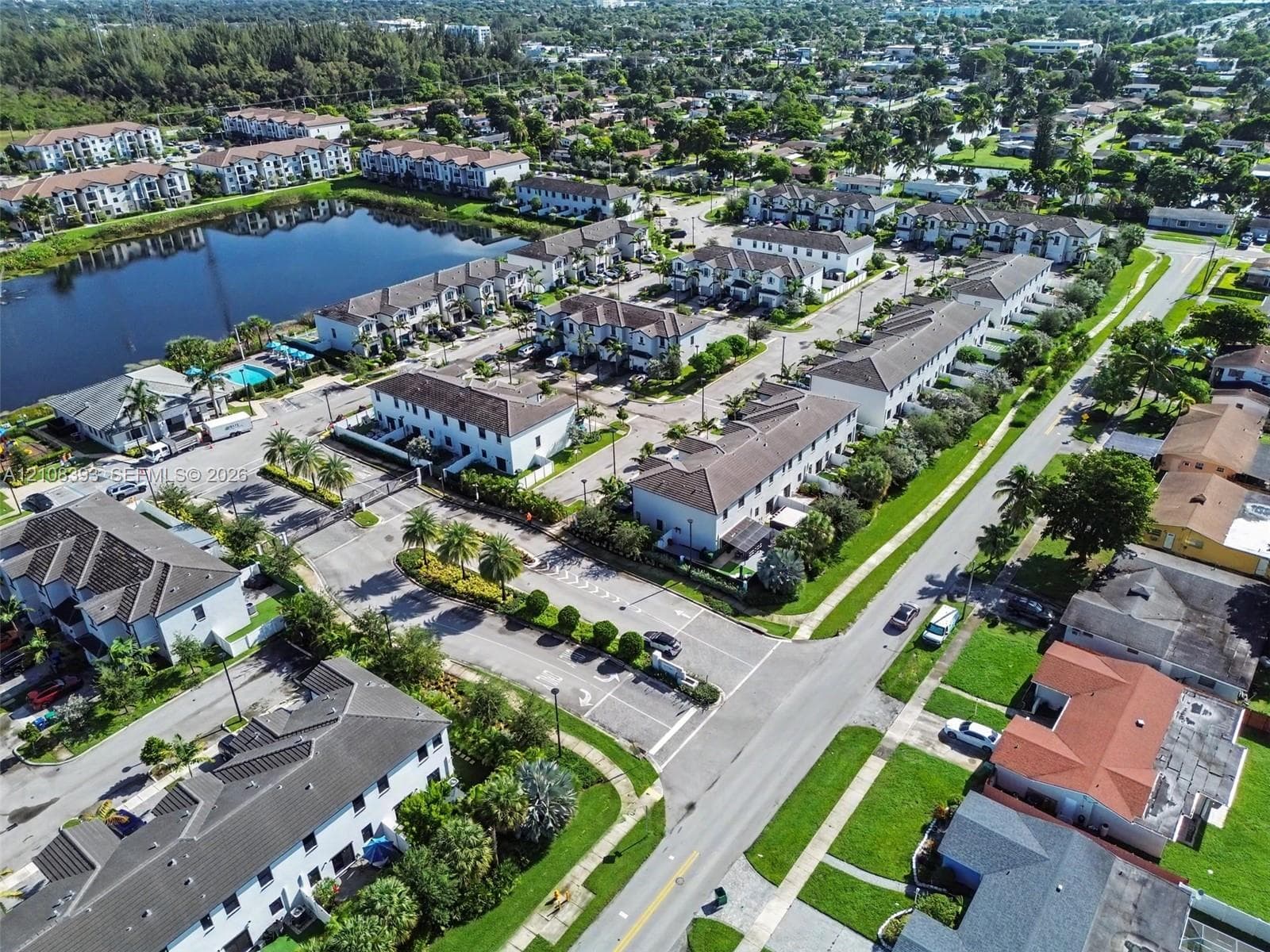 Aerial perspective of a multi-unit residential community featuring paved thoroughfares, organized parking, water features, and manicured landscaping