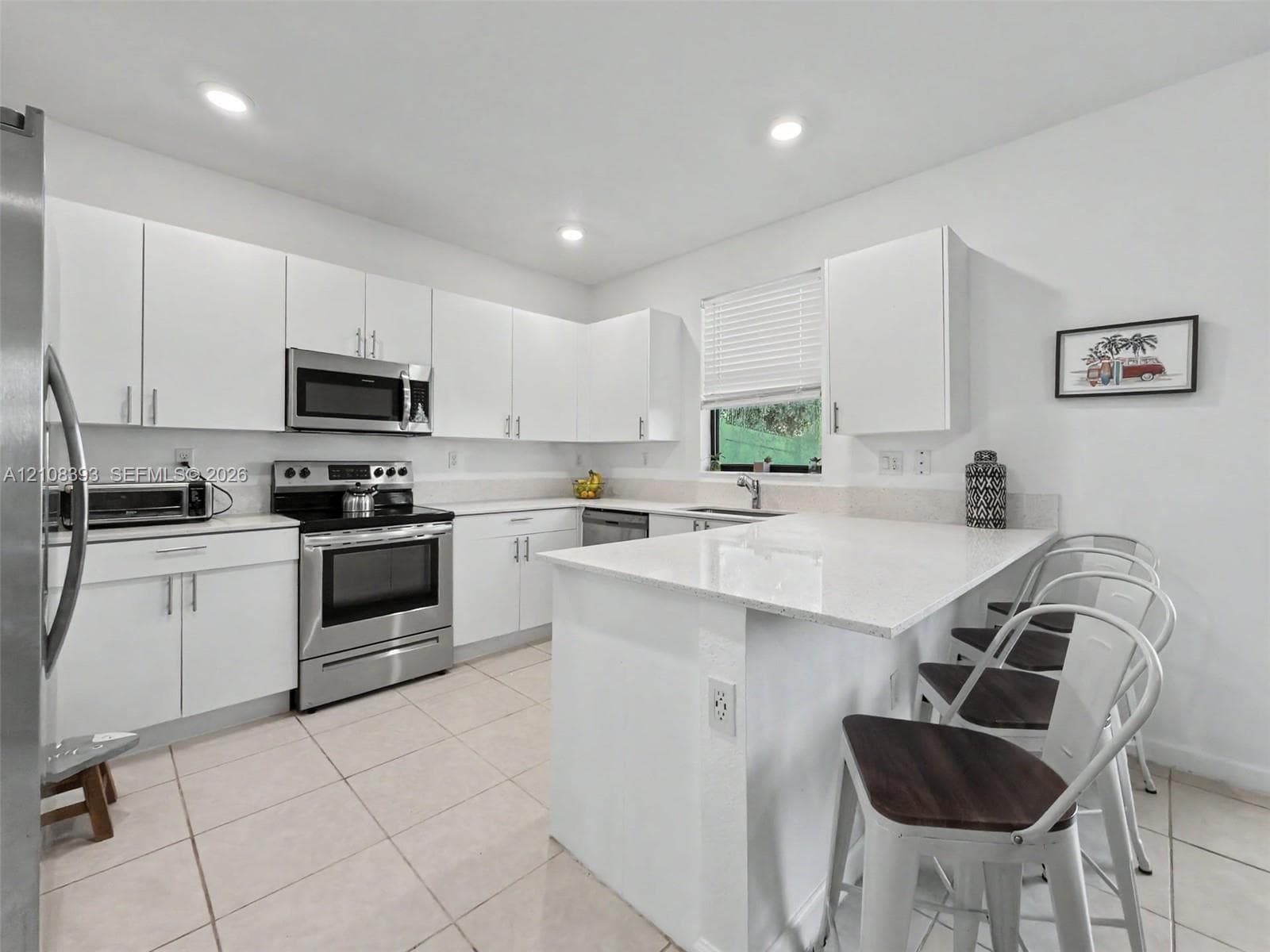 Kitchen featuring white flat-panel cabinetry, a peninsula with stone-finish countertops, stainless steel appliances, and large-format tile flooring