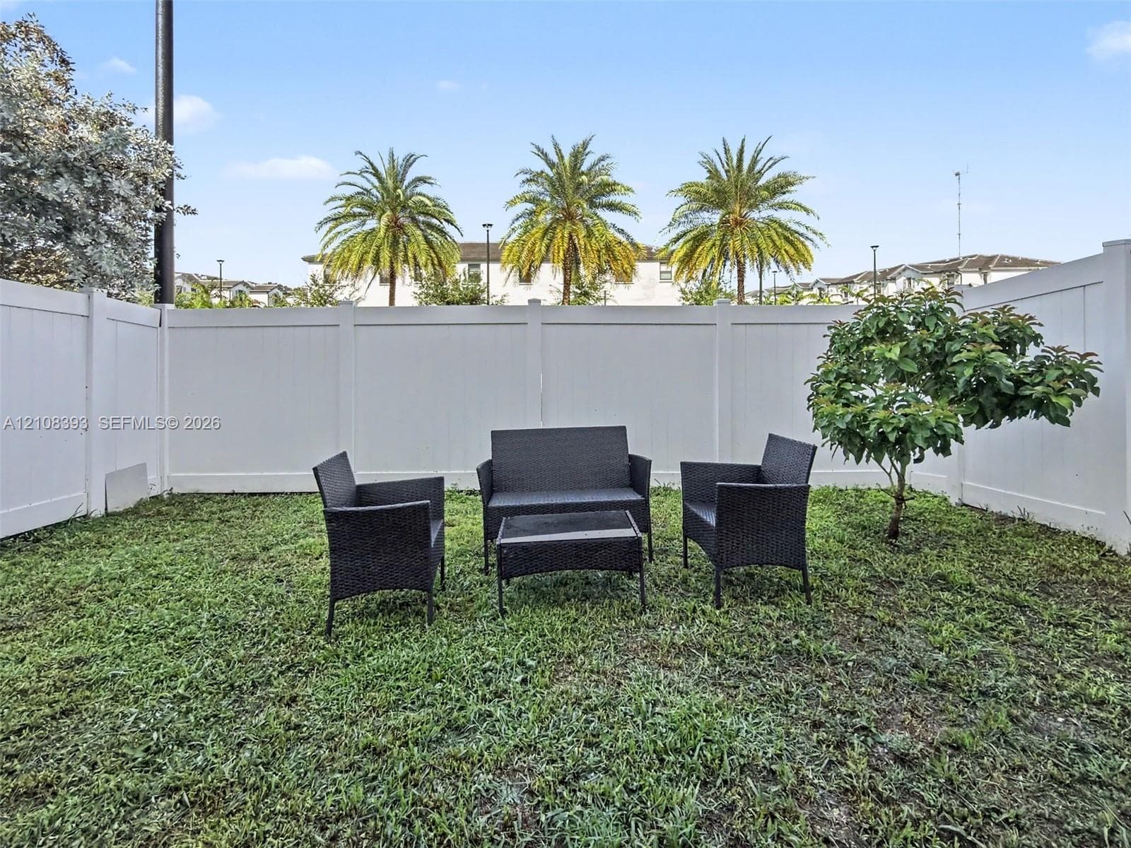 Enclosed backyard featuring white vinyl privacy fencing and a mature tree