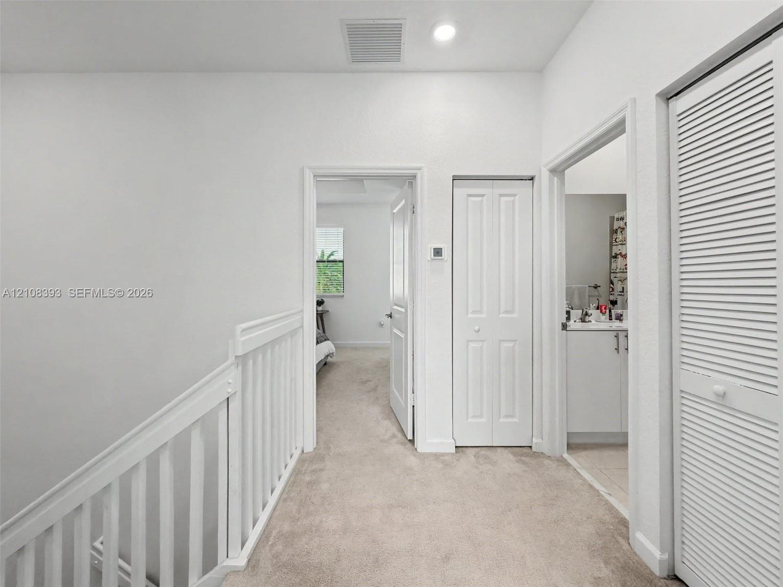 Hallway featuring neutral carpeting, white interior doors, a louvered closet door, and a white balustrade railing