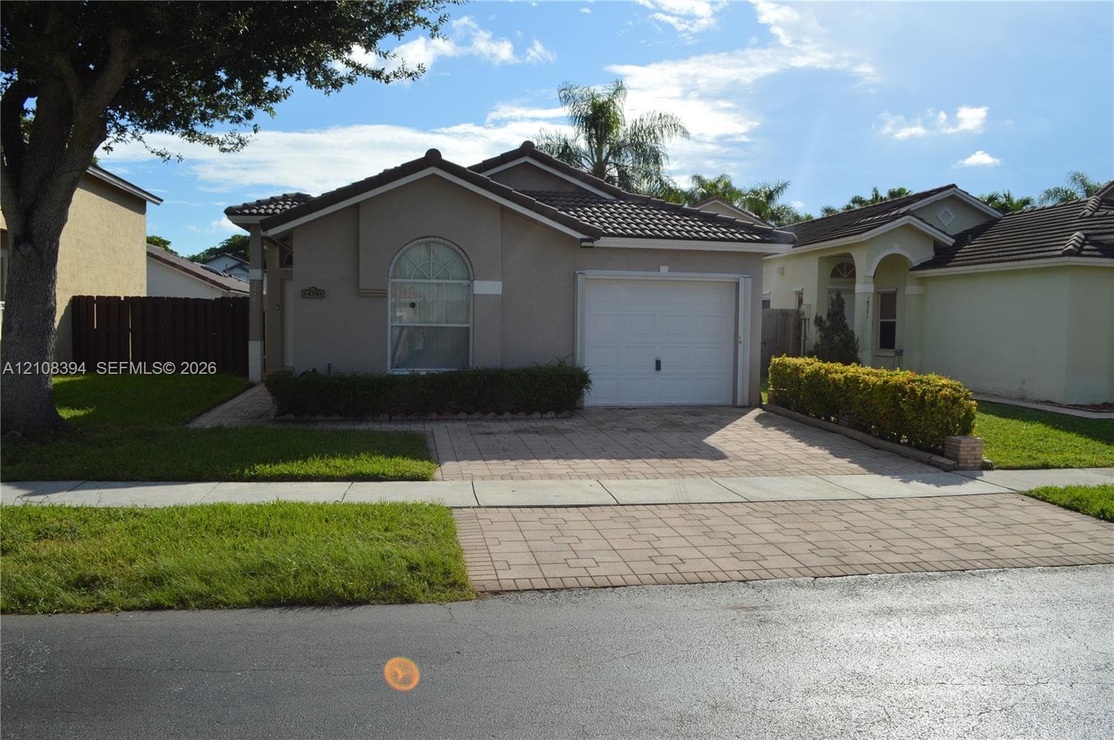 Single-story residence featuring a tile roof, neutral stucco exterior, arched window detail, and an attached garage with a paved driveway