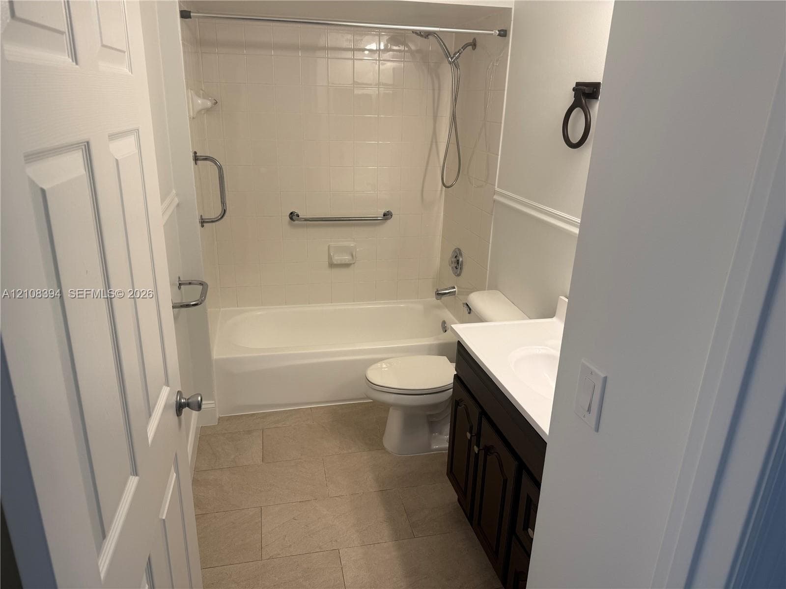 Bathroom featuring a deep-basin tub with a tiled surround, a dark wood-finish vanity with a white countertop, and stone-tile flooring