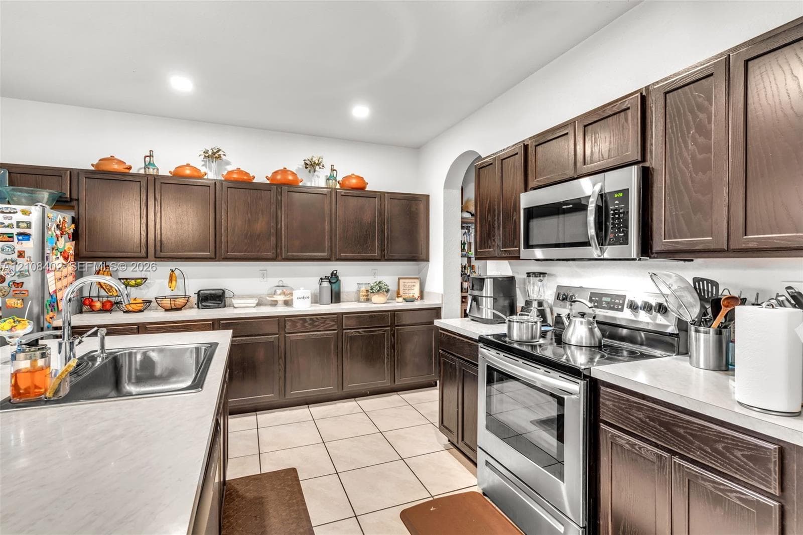 Kitchen featuring dark-stained cabinetry, stainless steel appliances, quartz countertops, a double-basin stainless steel sink, and tile flooring