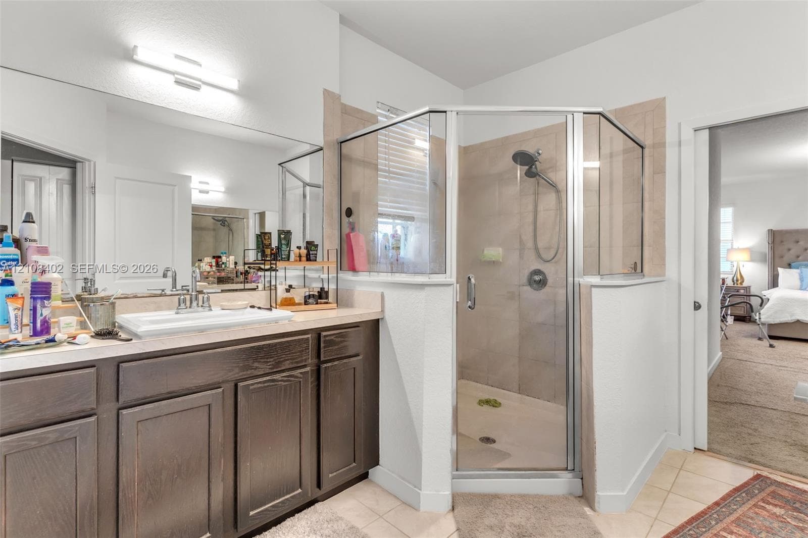 Bathroom featuring dark wood-finish cabinetry, a rectangular sink with a chrome faucet, a large wall-mounted mirror, and a corner shower enclosure with tile wall surround
