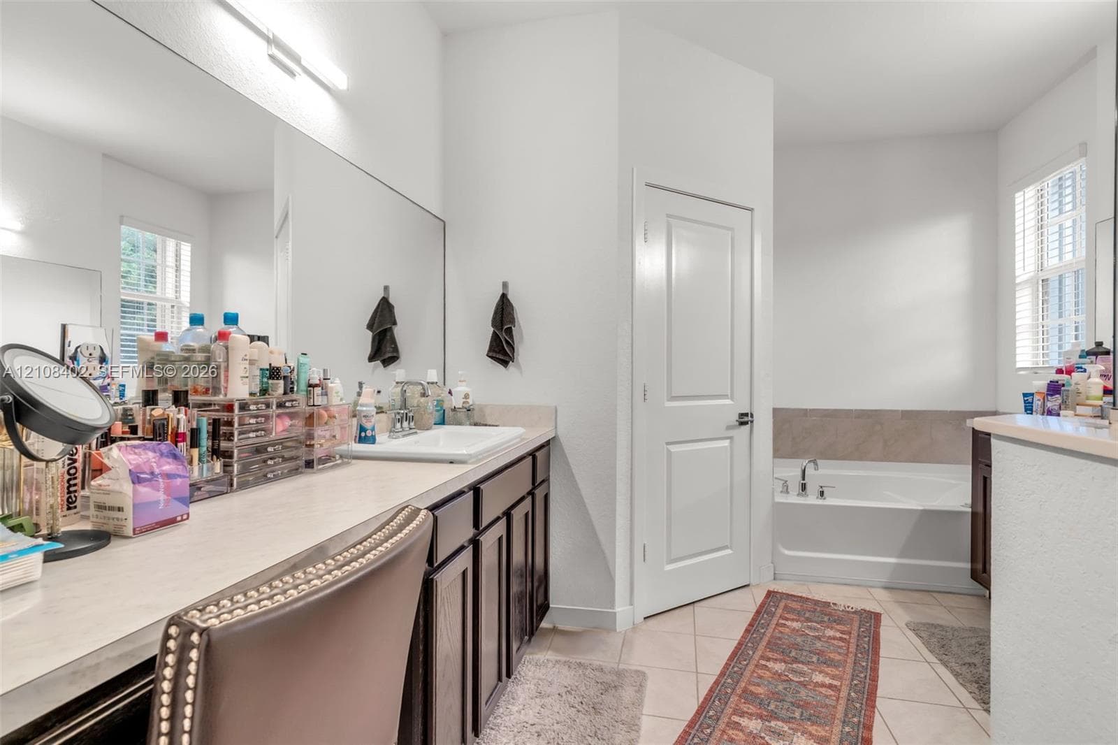 Bathroom featuring an expansive vanity with dark-finish cabinetry, a large wall-to-wall mirror, a rectangular drop-in sink, and a separate soaking tub with tiled surround