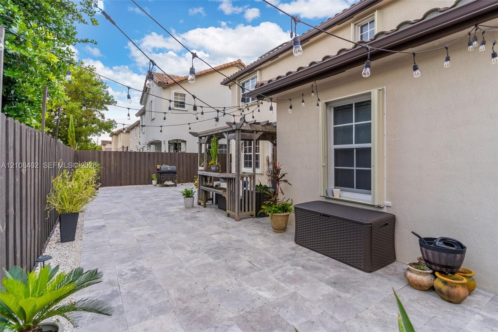 Paved patio featuring stone tile surfacing, wood-slat perimeter fencing, a built-in wooden pergola, and overhead string lighting