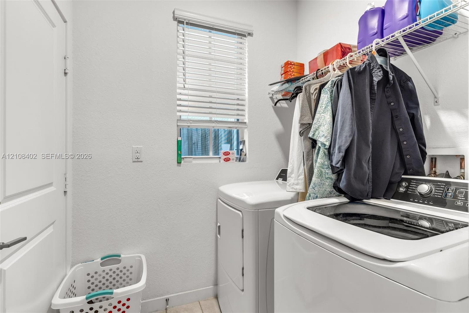 Laundry space featuring a window with horizontal blinds, wall-mounted wire shelving, and neutral wall finish