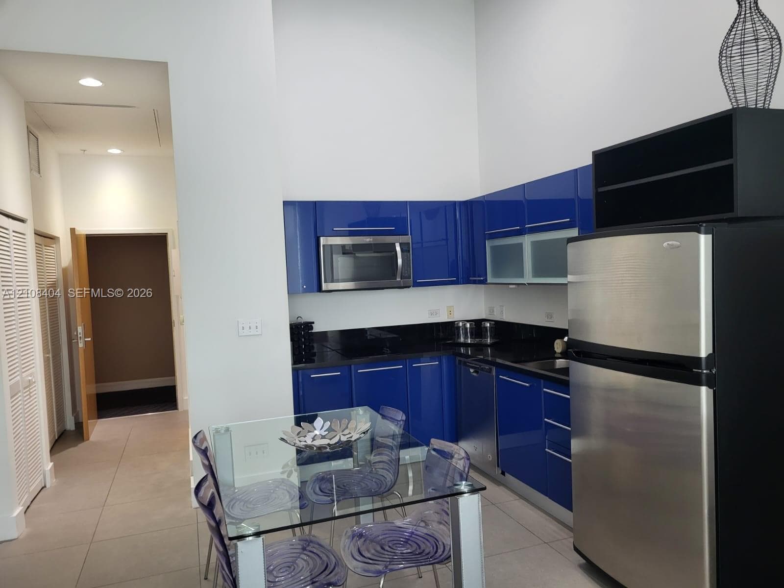 High-gloss blue cabinetry with integrated stainless steel appliances, dark stone countertops, and tile flooring