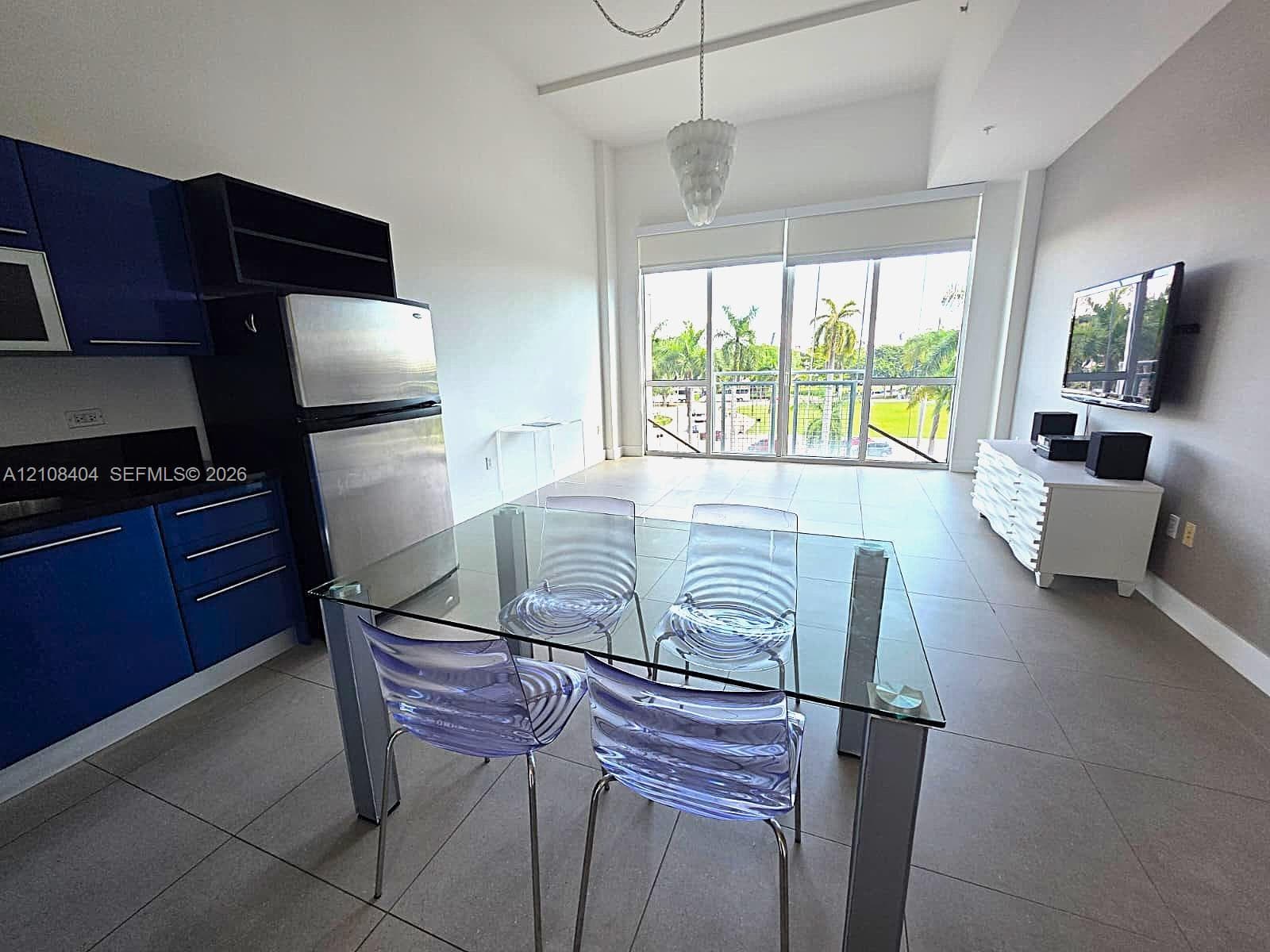 Open-concept kitchen featuring high-gloss blue cabinetry, stainless steel appliances, floor-to-ceiling windows, and tile flooring