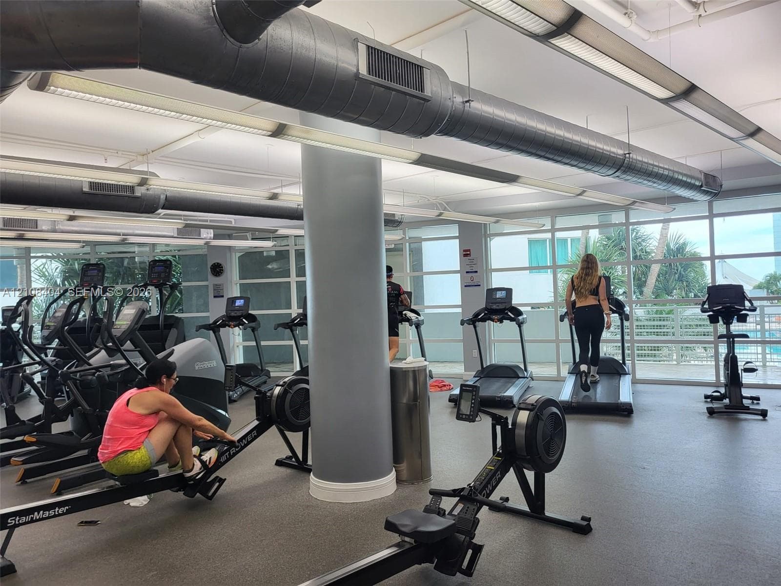 Fitness center featuring industrial-style exposed ductwork, floor-to-ceiling windows, and resilient rubberized flooring