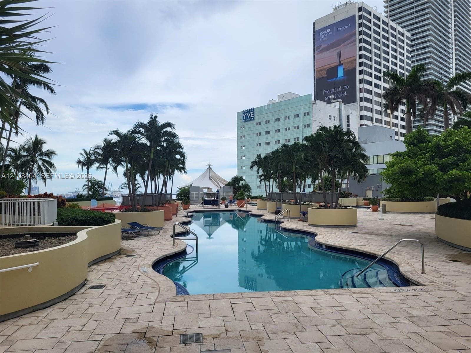 Curved swimming pool with built-in entry steps, stone paver decking, raised masonry planters, and mature palm trees
