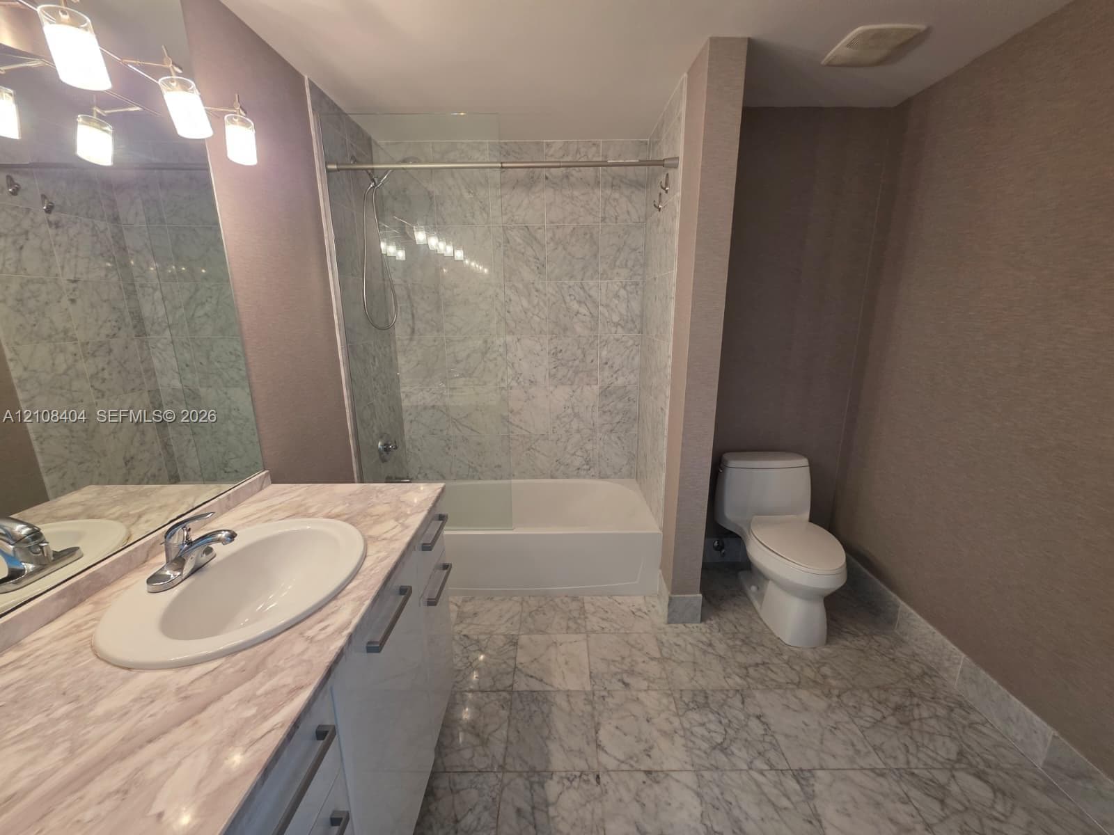 Bathroom featuring stone-finish flooring and tile-surround tub, vanity with stone-finish countertop and integrated sink, and multi-bulb vanity lighting