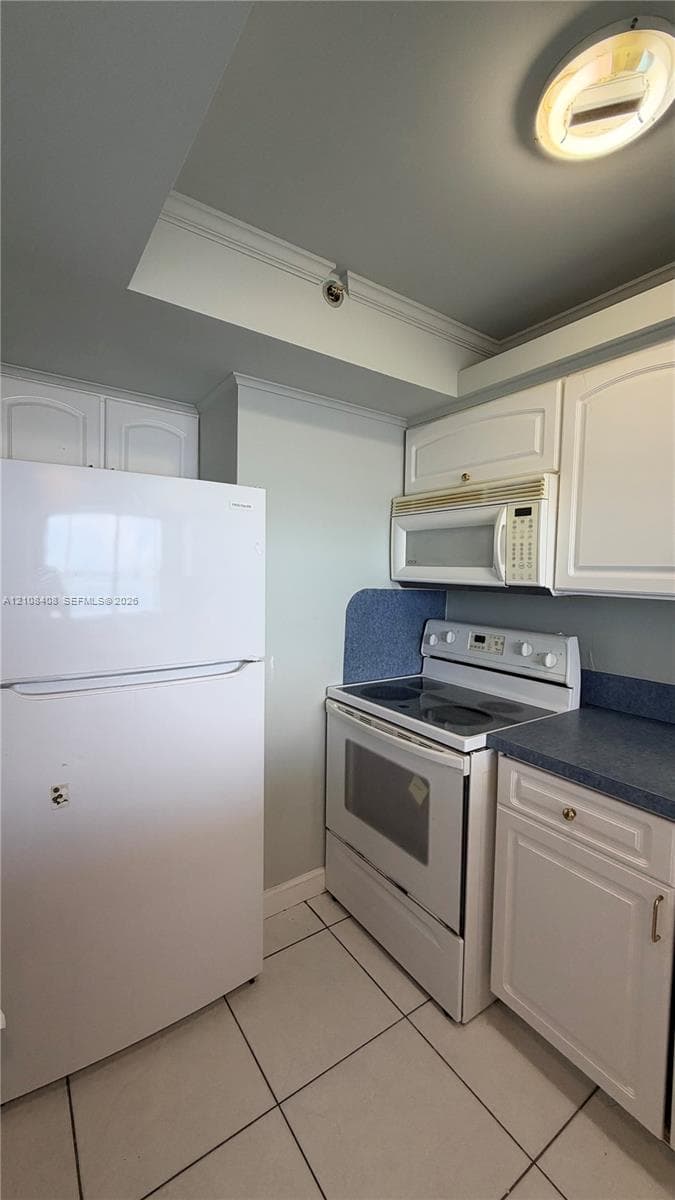 Kitchen featuring white cabinetry, solid-surface countertops, tile flooring, and built-in appliances including a refrigerator, electric range, and over-the-range microwave