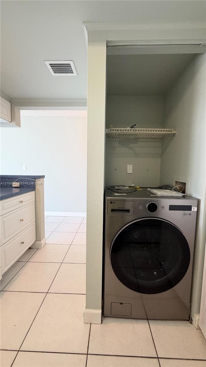 Laundry alcove featuring a stainless steel front-load washer, wire shelving, and neutral floor tile
