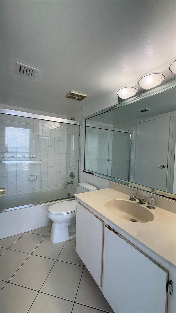 Bathroom featuring a vanity with integrated sink, large wall-mounted mirror, sliding glass shower enclosure, tiled tub surround, and tile flooring