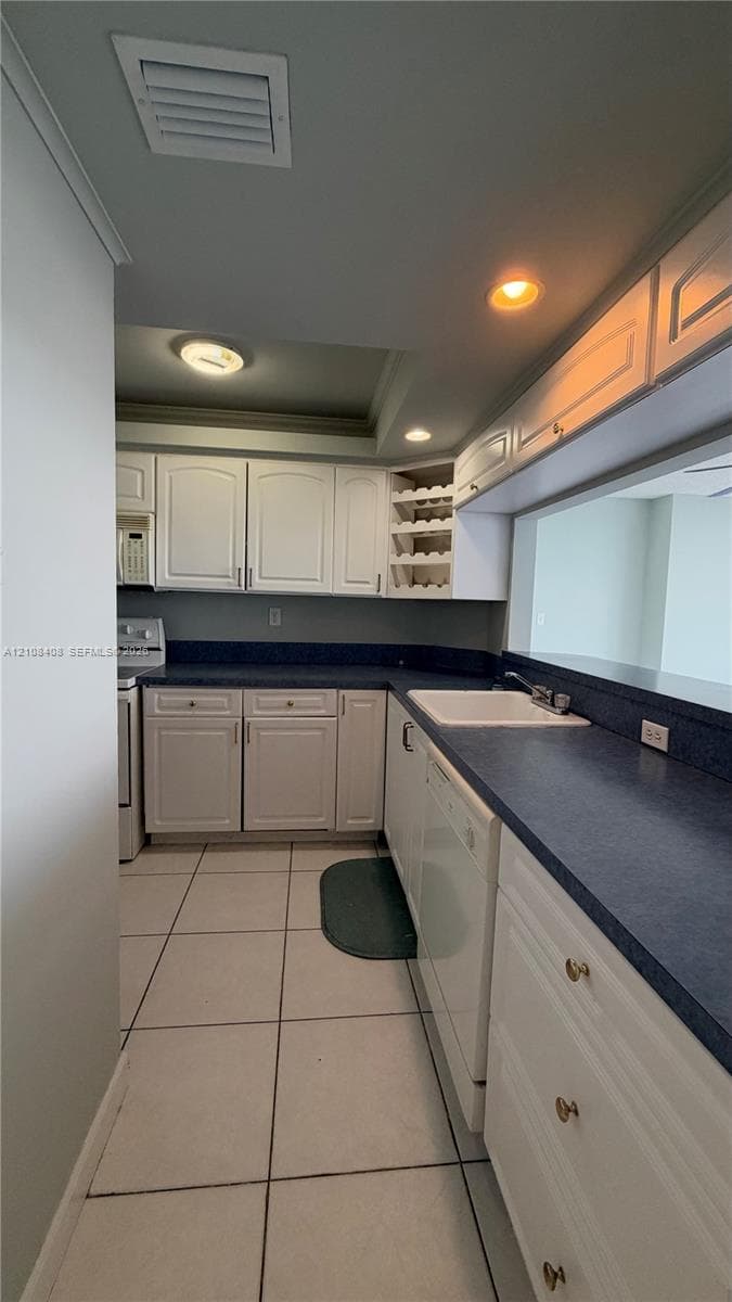 Kitchen featuring white cabinetry with integrated wine rack, solid-surface countertops, white porcelain sink, tile flooring, and recessed lighting